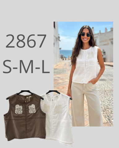 Mujer sonriente con blusa blanca y pantalones claros, fondo de mar y edificios.