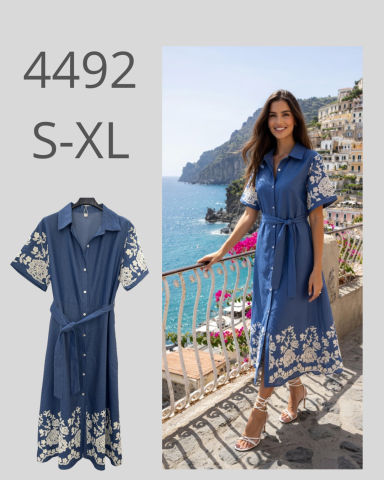 Vestido azul con bordado blanco, modelo en un paisaje costero.