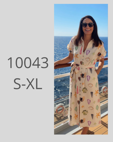 Mujer sonriente con gafas de sol, vistiendo un vestido largo junto al mar.