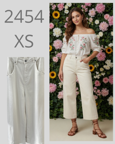 Mujer posando con blusa blanca bordada y pantalones claros frente a fondo floral.