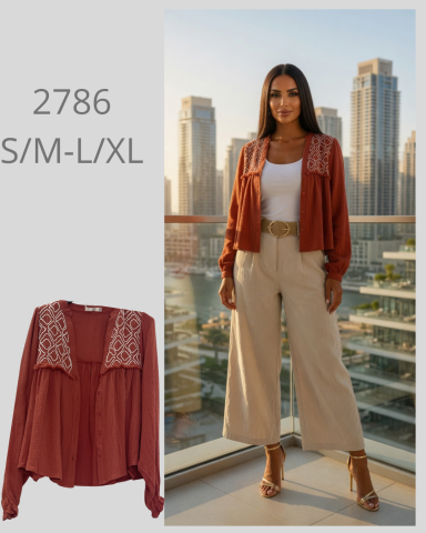 Modelo con blusa marrón y pantalones claros, fondo de ciudad moderna.