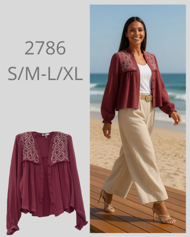 Mujer caminando por la playa, vistiendo chaqueta burdeos y pantalones claros.