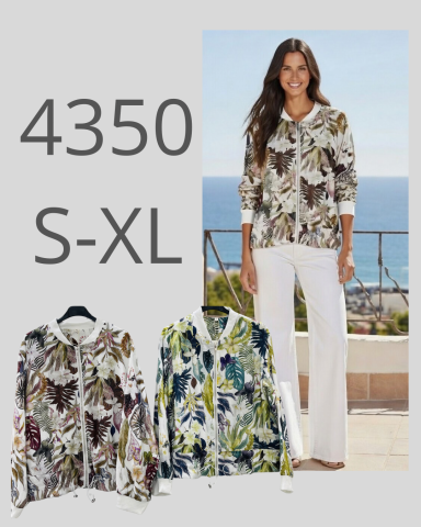 Mujer con blusa estampada y pantalones blancos, de pie frente al mar. 